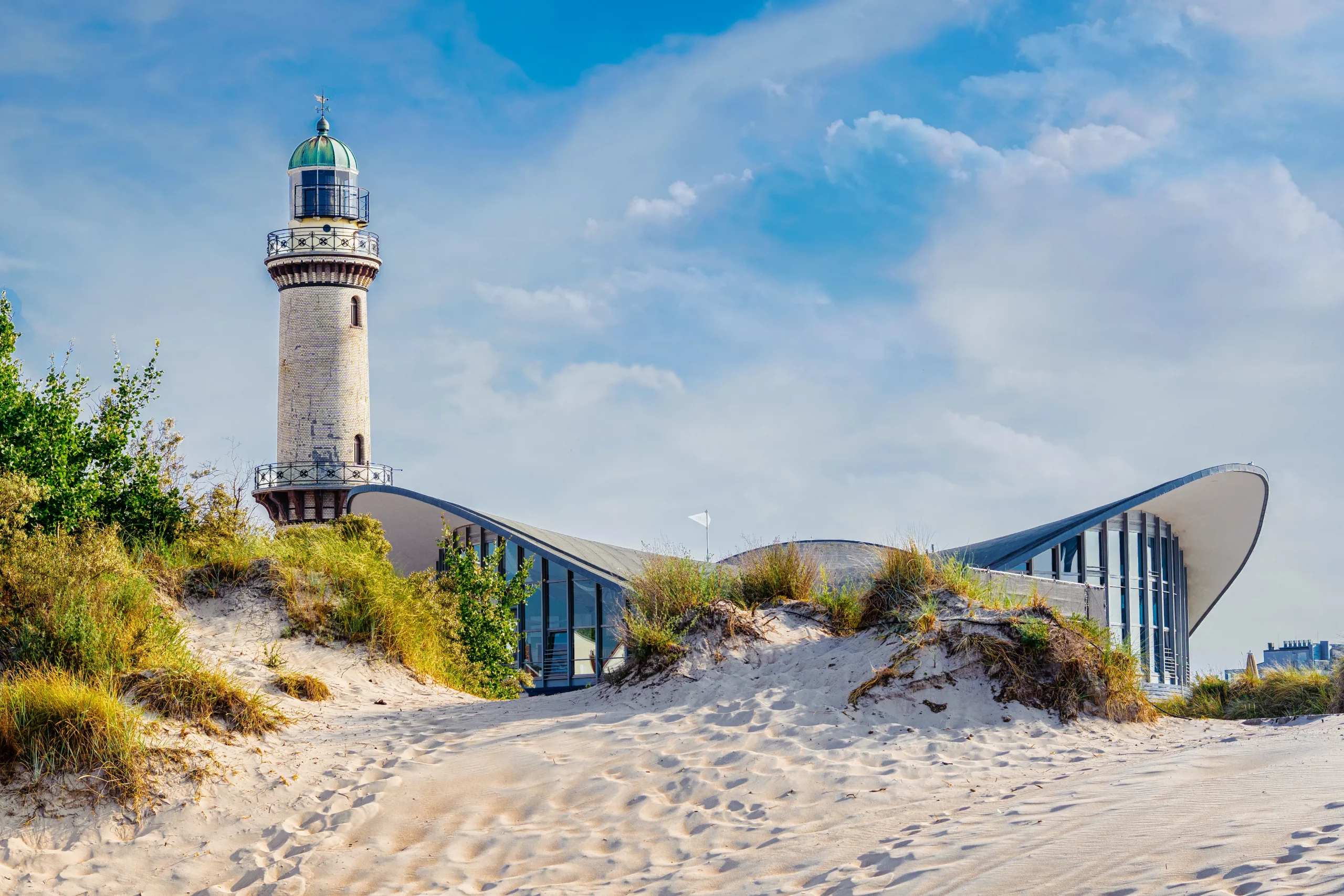 Düne mit Blick auf Leuchtturm und Gebäude mit geschwungenem Dach
